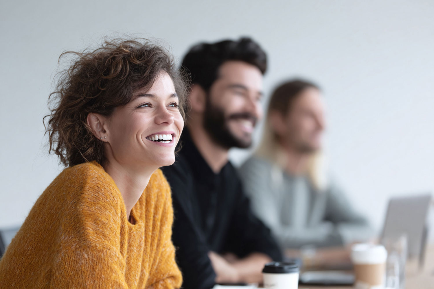 Un groupe de jeunes professionnels sourient en écoutant et regardant quelqu'un hors-champ.